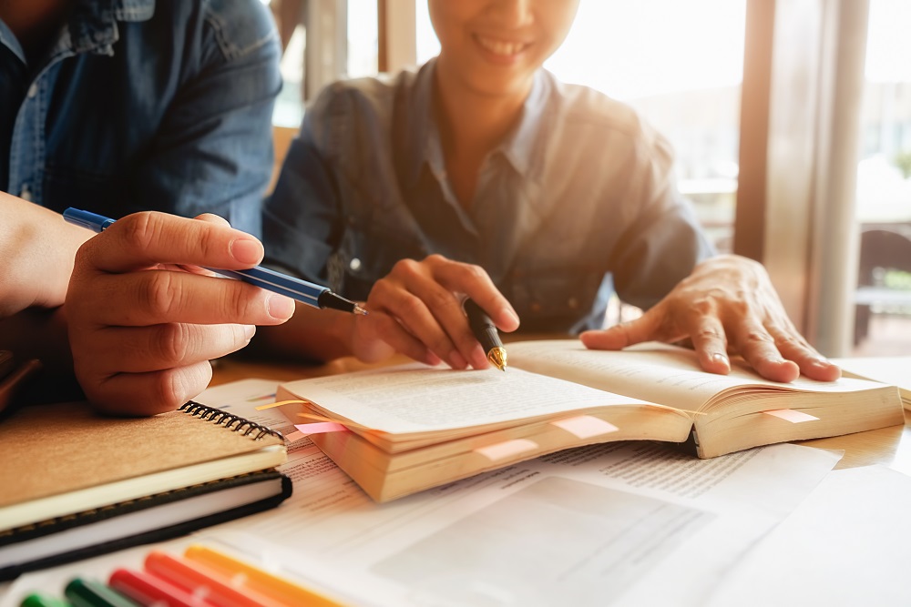 5 passos para fazer um bom planejamento de gestão escolar: A imagem mostra duas pessoas com uma caneta na mão, analisando um livro.
